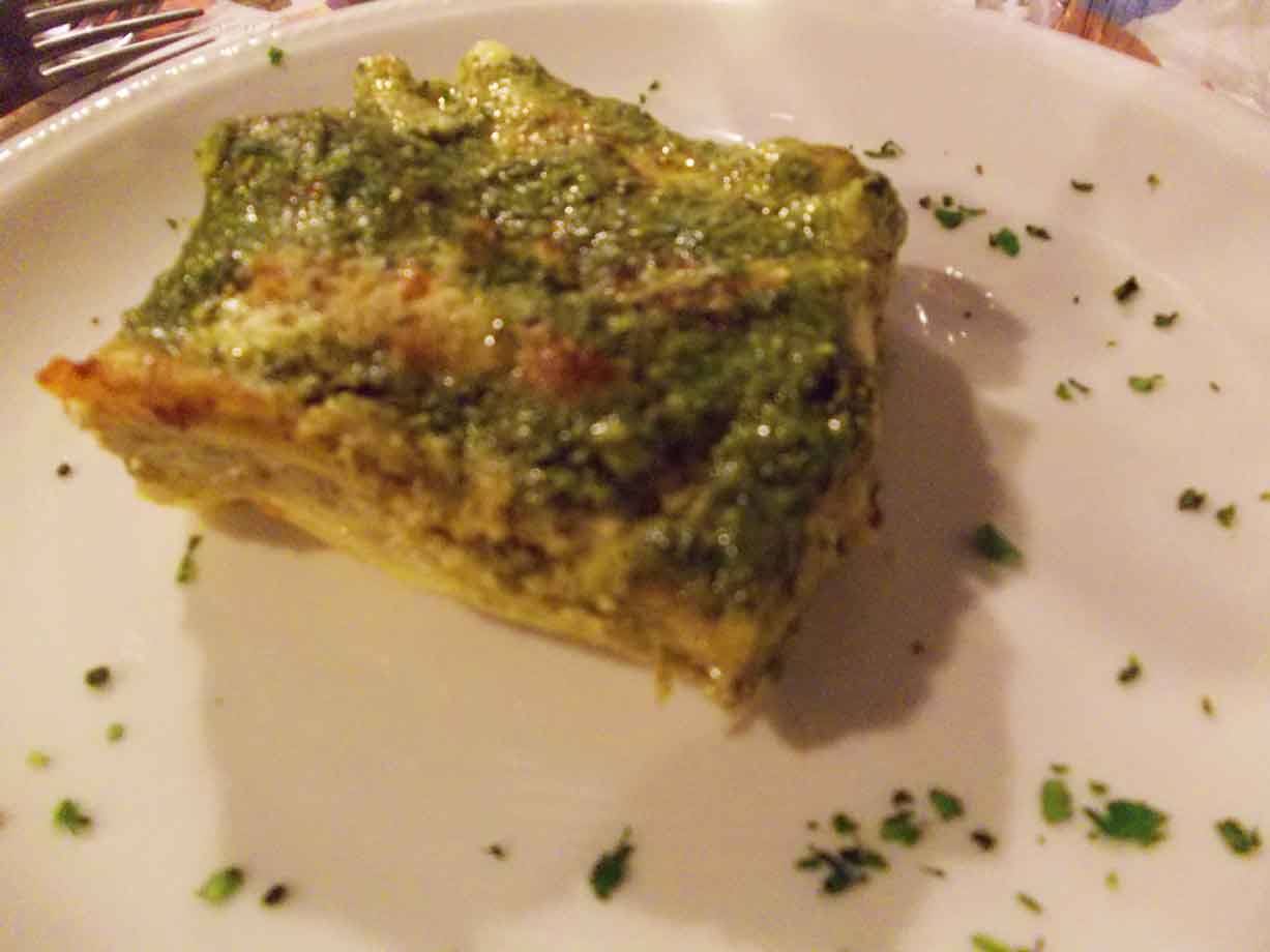 Lasagna al pesto servita su piatto bianco, luce calda da ristorante