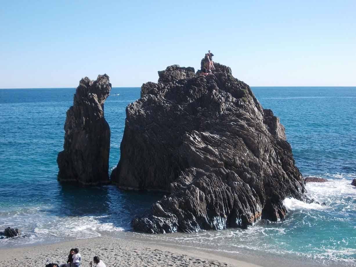 Turisti in cima allo scoglio di Monterosso, onde sull'arenile sotto