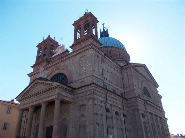 Novara Cathedral in brick with copper dome, bell towers, bright sunlight