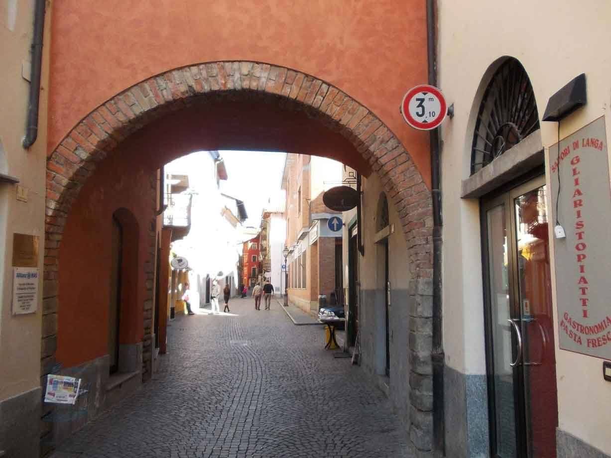 Arco di mattoni su vicolo ciottolato con pedoni, insegna Gastronomia Gagliardi