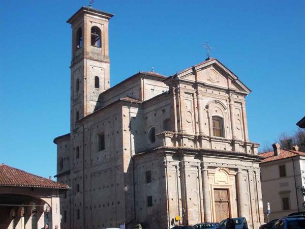 Stone church with tall bell tower, parked cars under blue sky