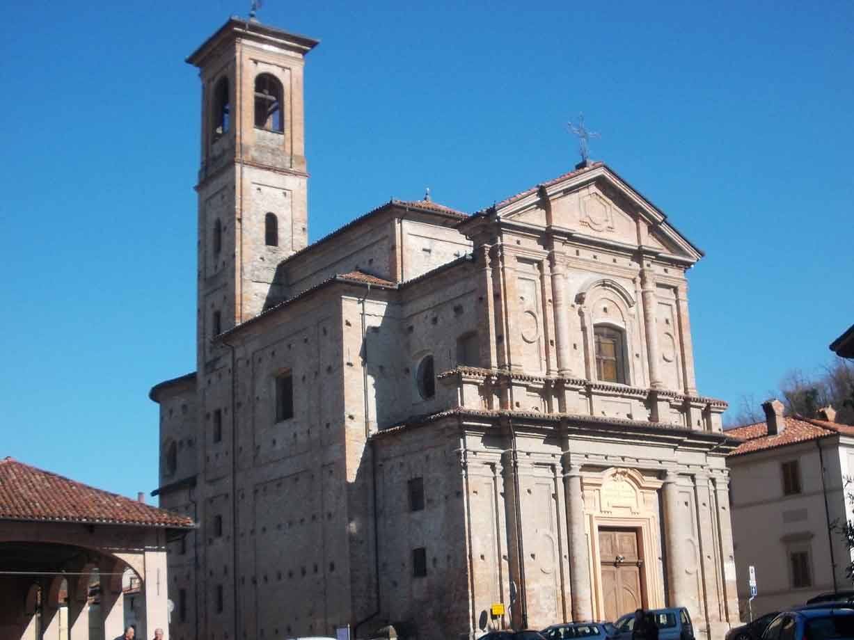 Chiesa in pietra con alto campanile, automobili parcheggiate sotto cielo azzurro