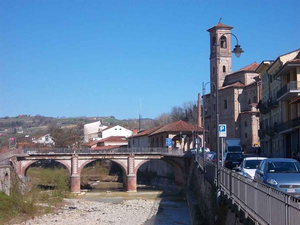 Brick bridge over dry riverbed, bell tower and parked cars along the road