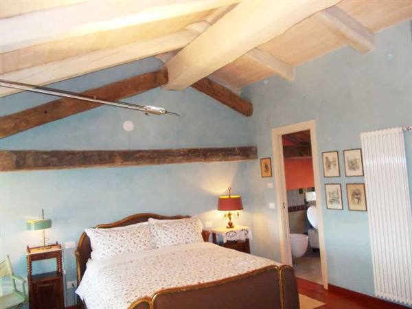 Bedroom with antique wooden bed, exposed beams, pale blue walls and lit lamp