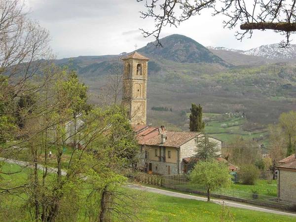 Stone bell tower among tile-roofed houses, green meadow and mountains