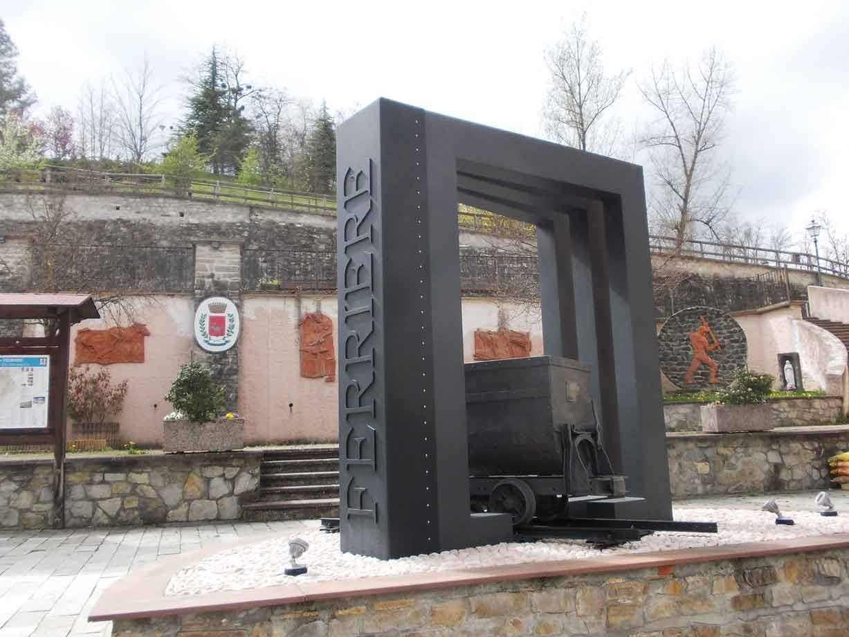Monumento in ferro con scritta Ferrière e carrello minerario su binario