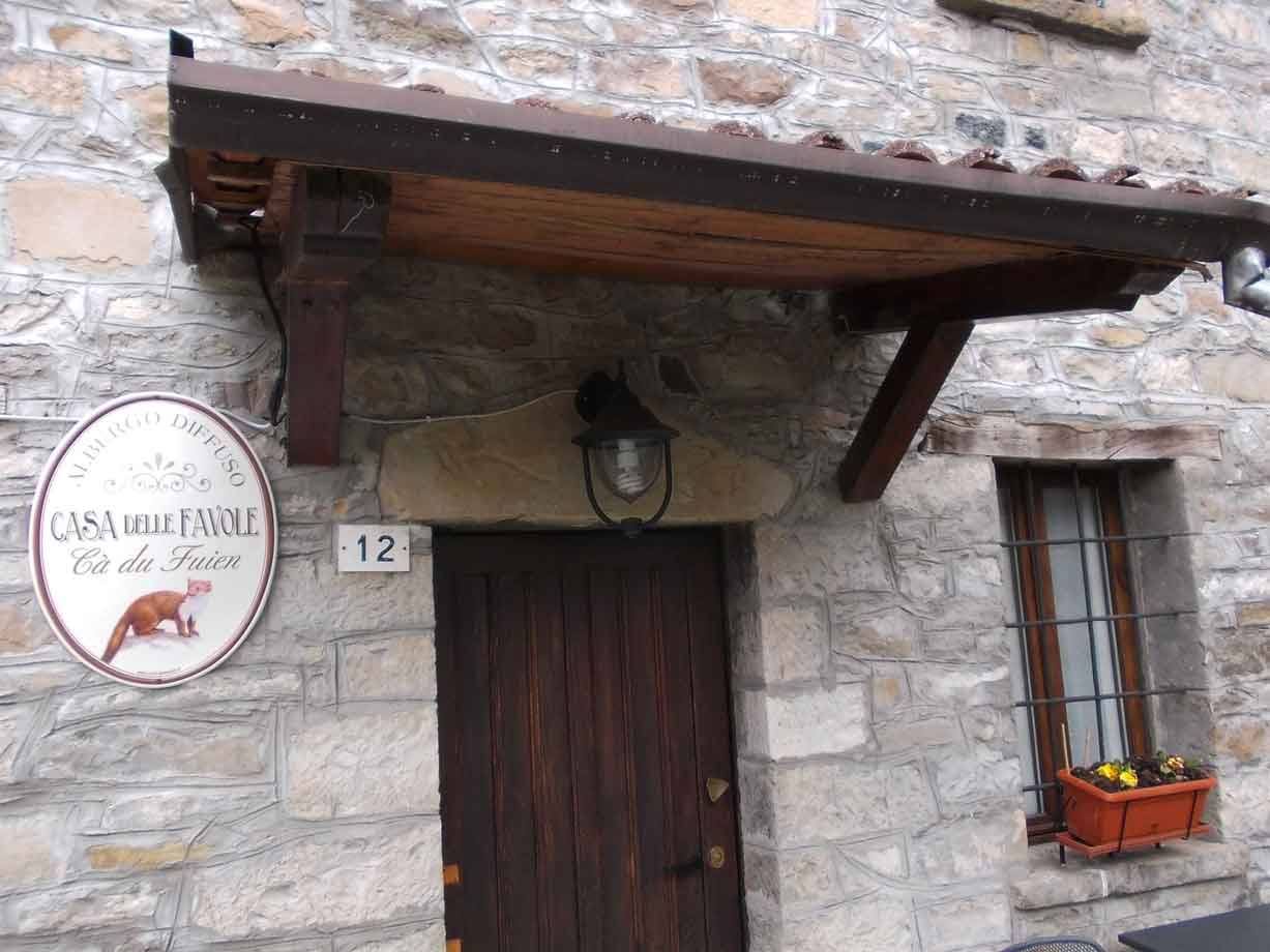 Ingresso in pietra con portale di legno, lanterna e insegna della Casa delle Favole