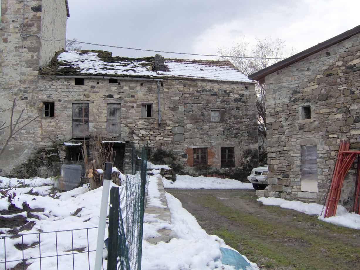 Vecchie case in pietra con neve sul tetto, piccolo cortile e furgone bianco