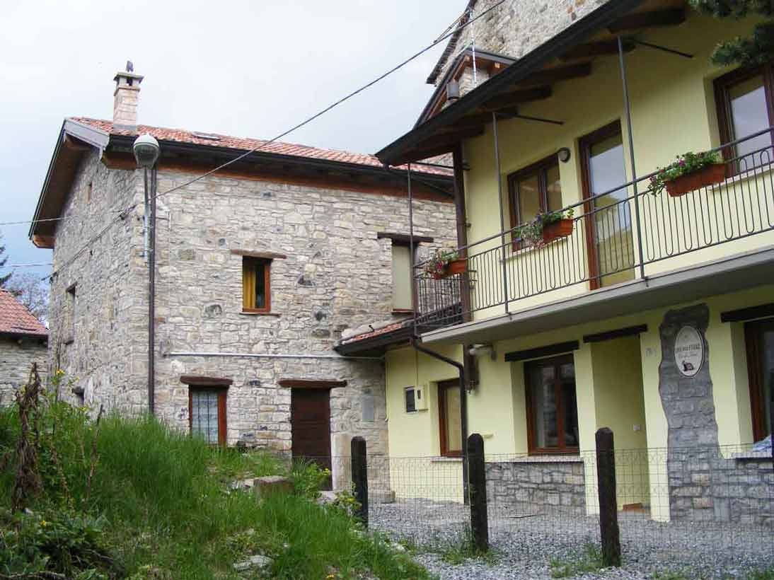Casa in pietra e edificio giallo con balcone in ferro, giardino verde