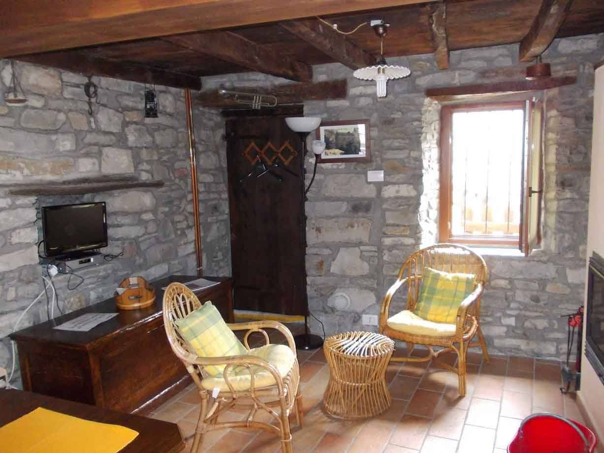 Soggiorno rustico con pareti in pietra, poltrone di vimini e travi in legno