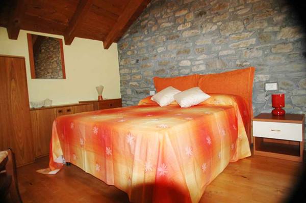 Bedroom with orange bedspread, white pillows, stone wall and wooden beams