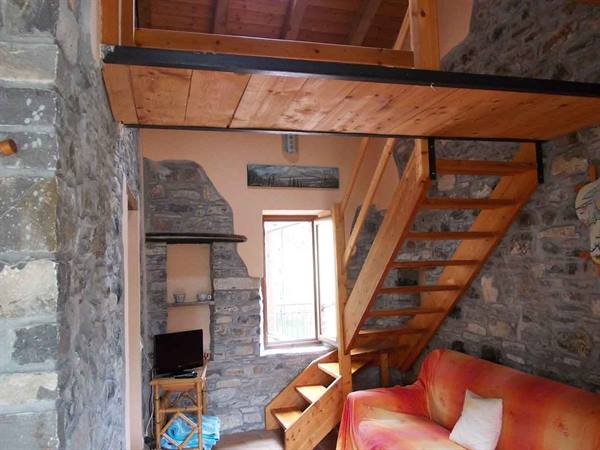 Stone interior with wooden staircase, loft and orange sofa beneath the window