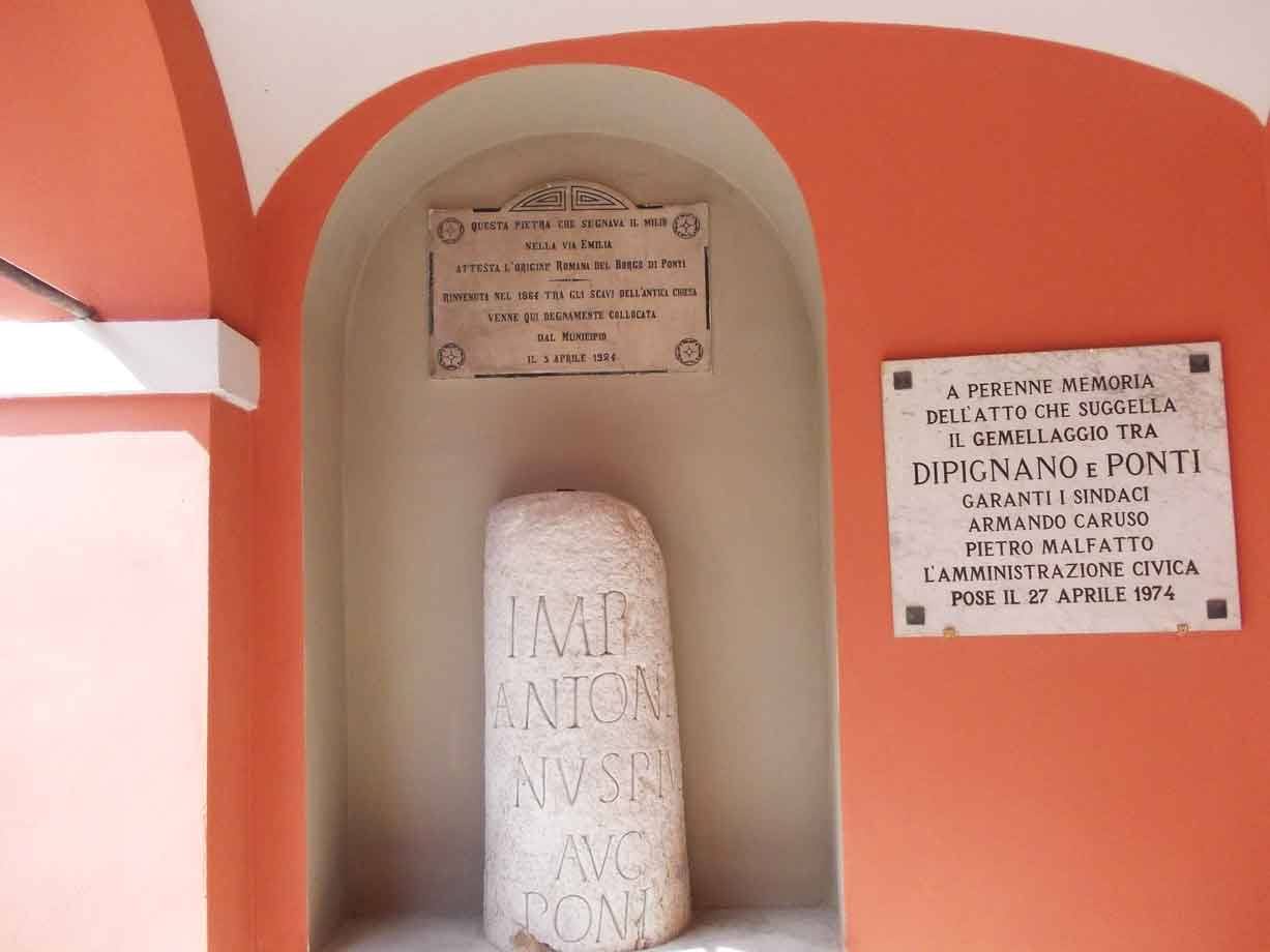 Cippo romano in pietra con iscrizione incassato in nicchia arancione con targhe marmoree