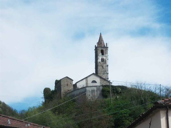 Stone church with tall bell tower on hill, cloudy sky, rooftops below