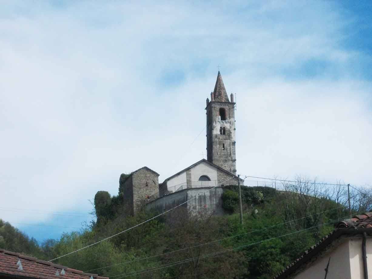 Chiesa in pietra con alto campanile sulla collina, cielo nuvoloso, tetti sottostanti