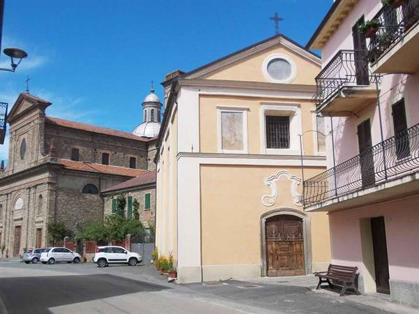 Yellow church with wooden portal and bench, stone church on the left