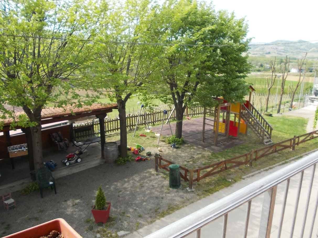 Cortile con parco giochi in legno, altalene e alberi verde brillante