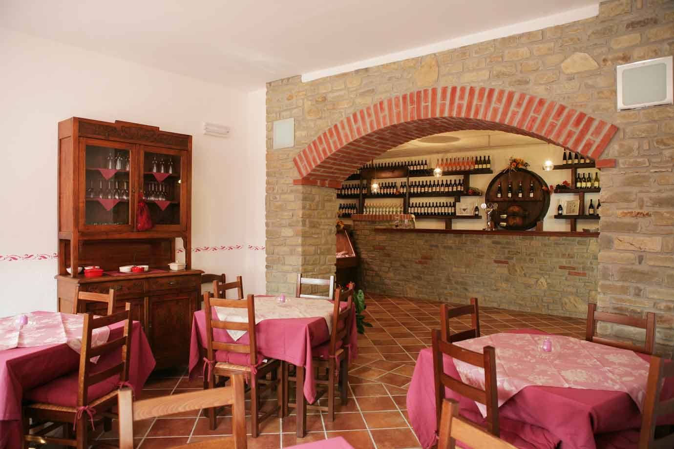 Sala di trattoria con tavoli a tovaglia rosa, muro in pietra, arco in mattoni e bar delle bottiglie