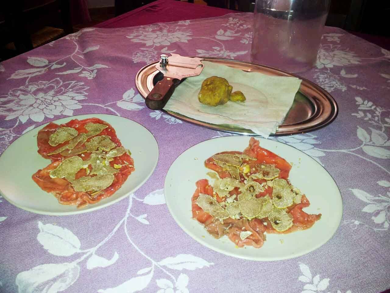 Carpacci con scaglie di tartufo, vassoio metallico e pelapatate su tovaglia lilla