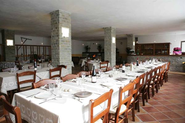 Restaurant dining room with long set tables, wooden chairs, stone pillars