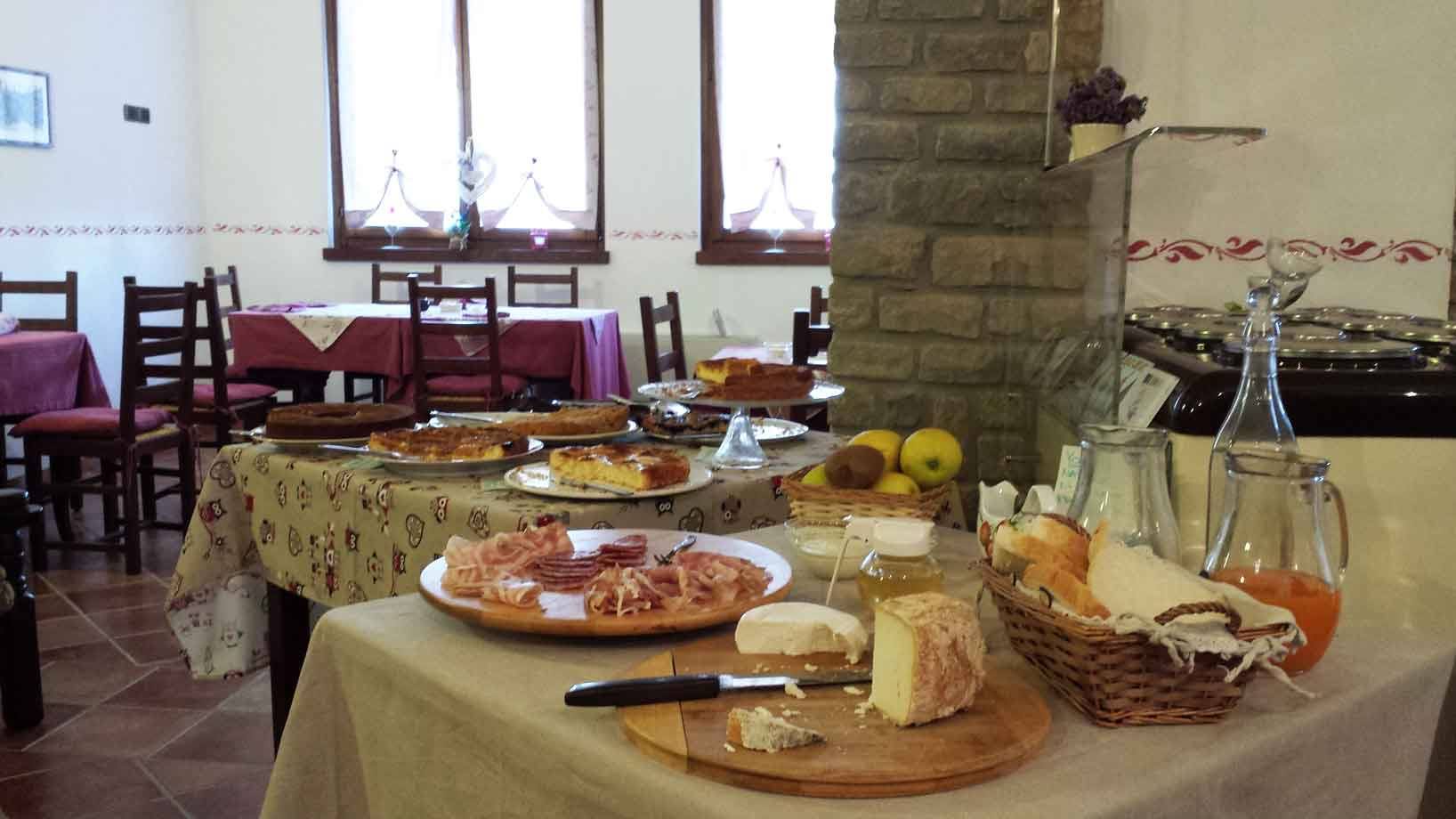 Colazione in sala rustica: formaggi, salumi, pane e succhi su tavoli imbanditi