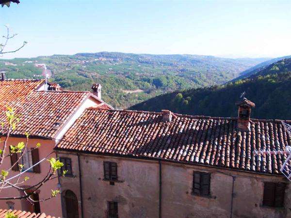 Terracotta tiled roofs of a stone village above green hills