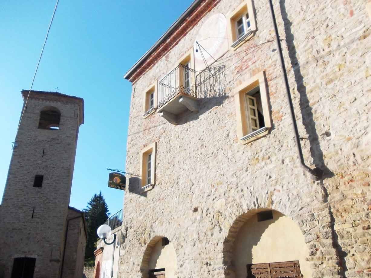 Palazzo in pietra con balcone e campanile medievale, cielo azzurro