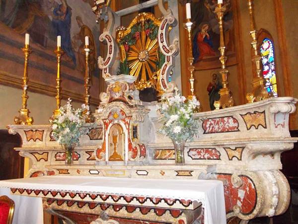 Polychrome marble high altar with white flowers and golden candlesticks inside a church