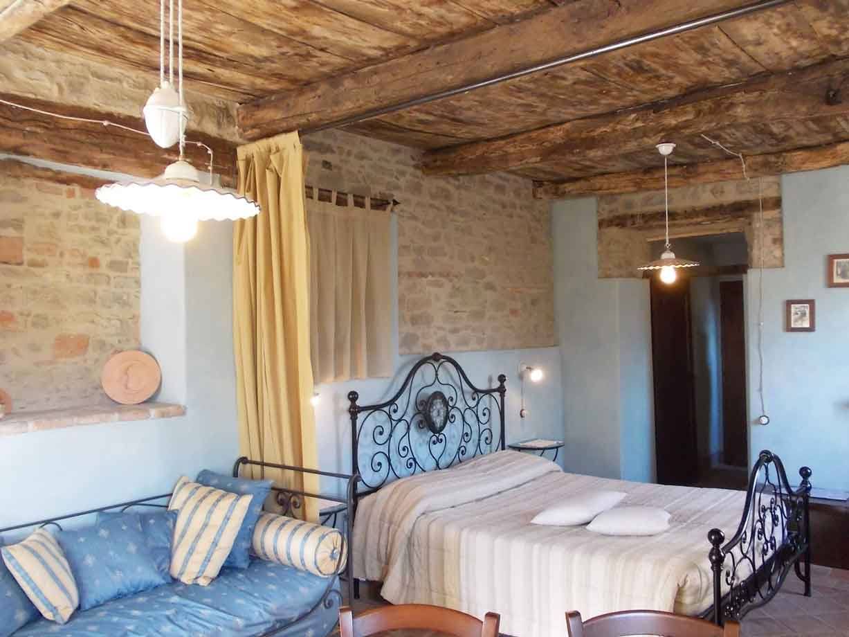 Camera rustica con letto in ferro battuto, travi in legno e muri di pietra