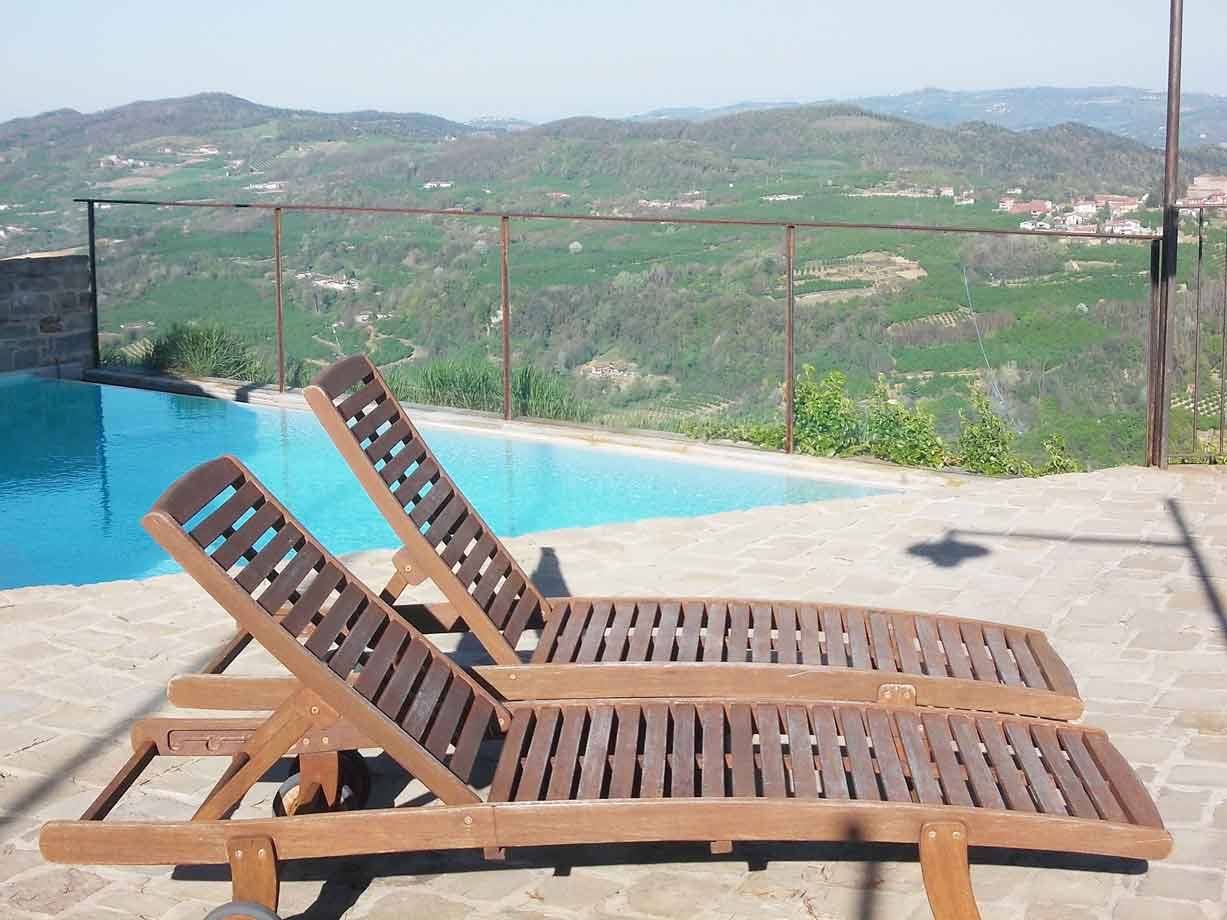 Due lettini di legno vuoti accanto a una piscina sopra le colline coltivate