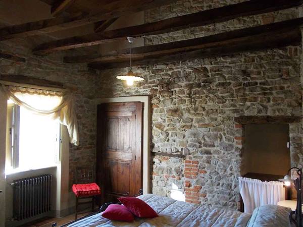 Bedroom with stone walls, wooden beams, bed and red pillows