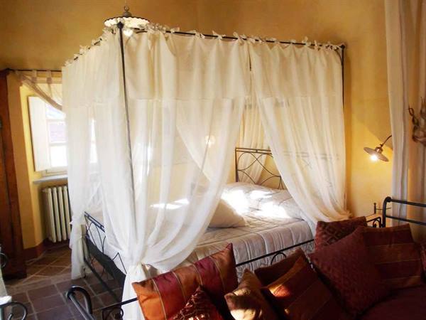 Bedroom with wrought iron canopy bed, white drapes and orange pillows