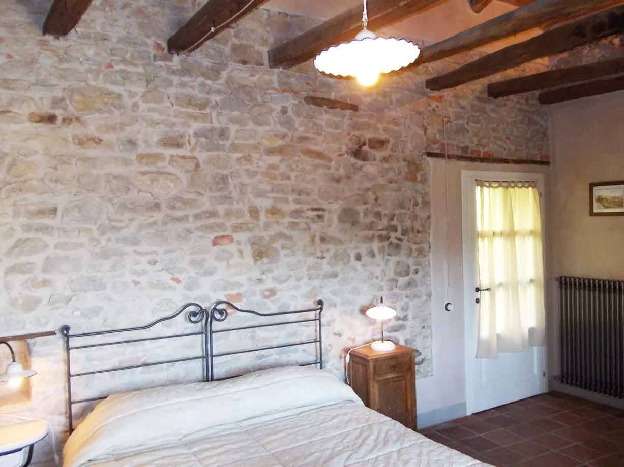 Camera con letto in ferro battuto e muro in pietra a vista con travi in legno
