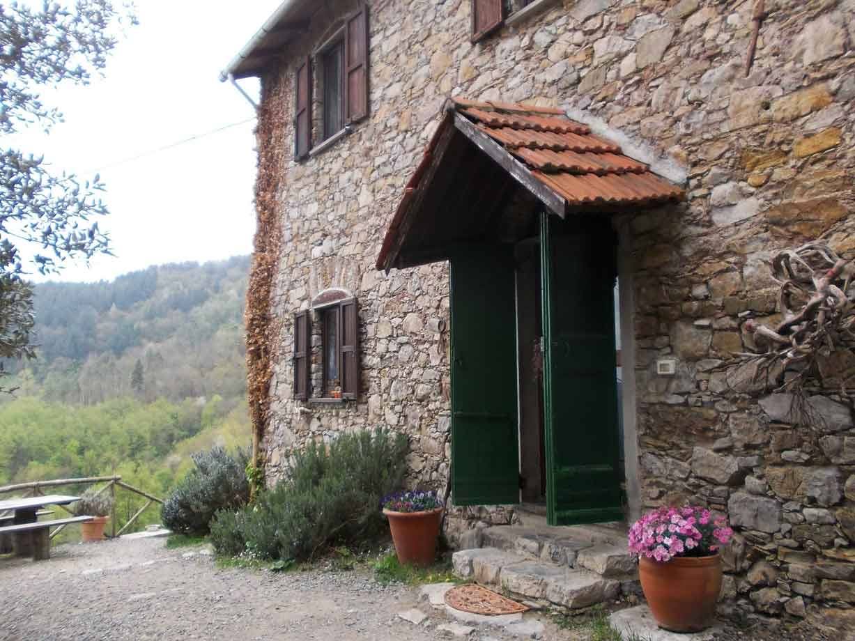 Casa rurale in pietra con porta verde, tegole rosse e vasi di fiori rosa