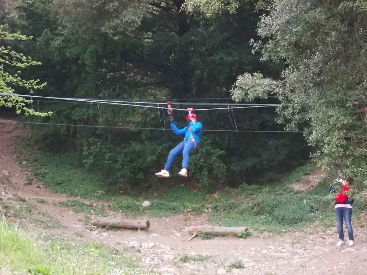 Ragazzo in giacca blu scende su una zip line tra gli alberi