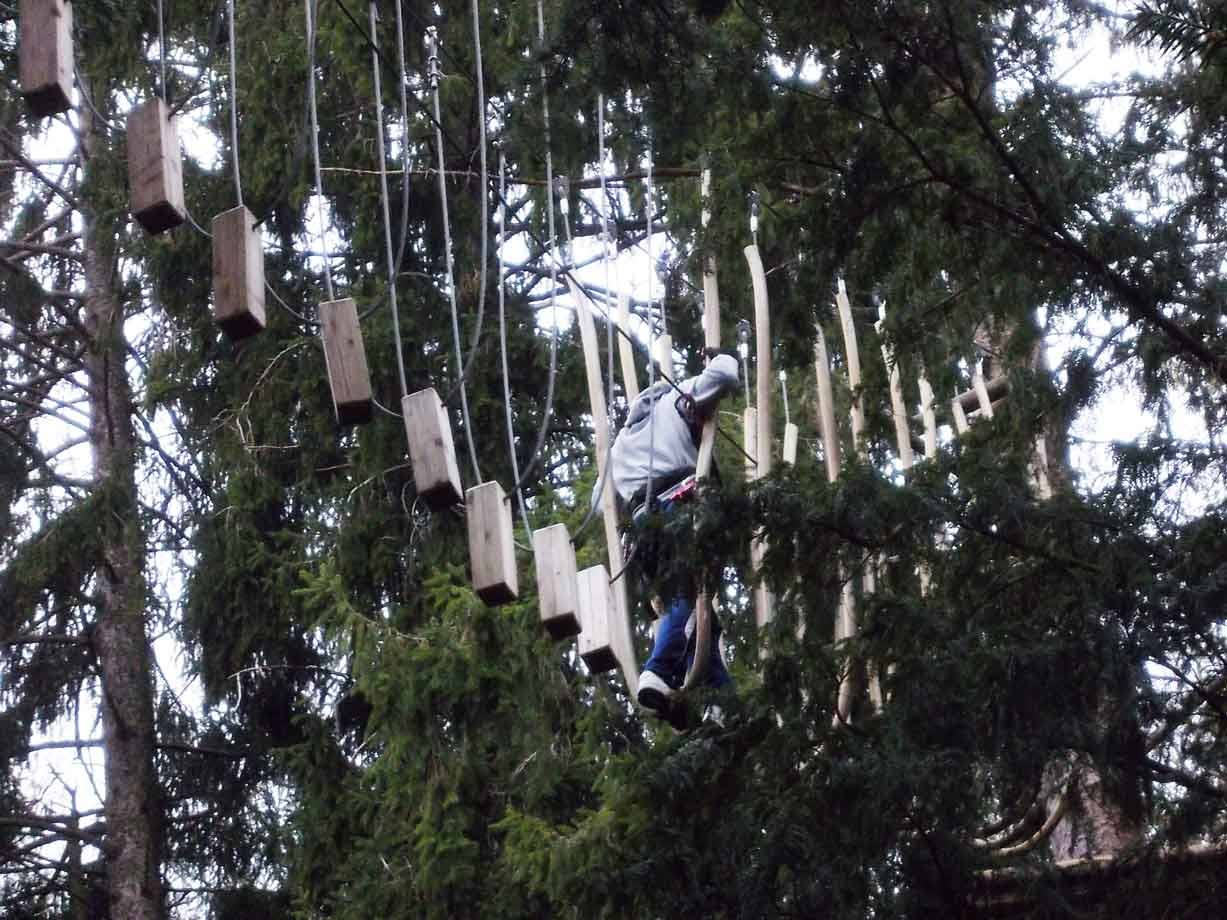 Ragazzo con casco attraversa tronchi sospesi tra abeti nel parco avventura