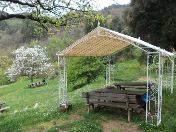 White wrought iron gazebo with wooden picnic tables on a green hillside