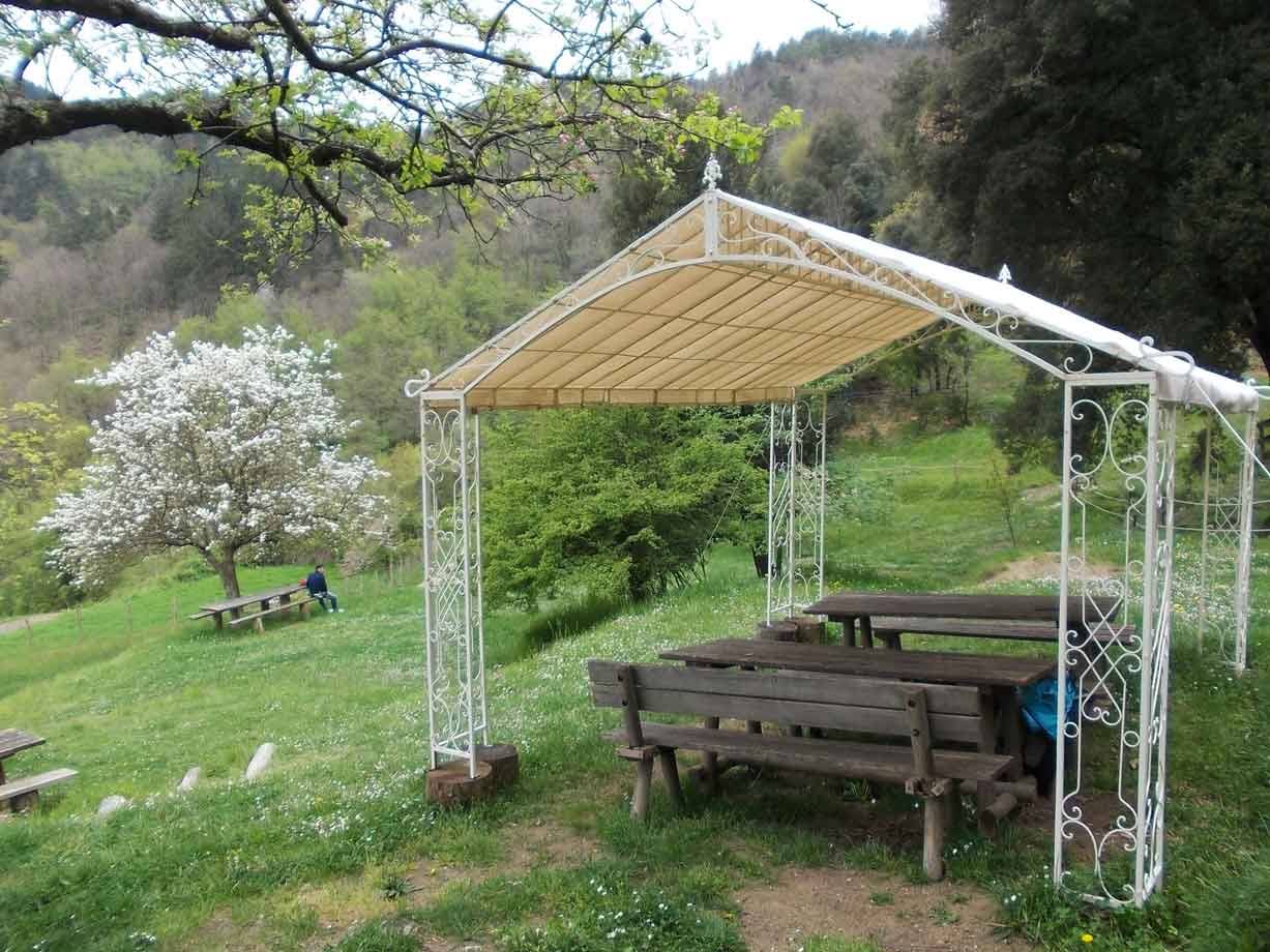 Gazebo in ferro battuto bianco con tavoli di legno su prato verde in collina