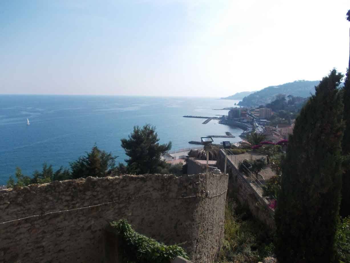 Muro in pietra e cipresso sopra la costa ligure, mare azzurro con vela