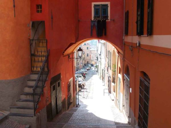 Stone stairway between orange houses, arch with hanging laundry, sunny alley