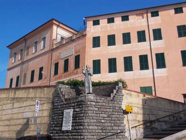 Monk statue on stone wall in front of pink building with green shutters