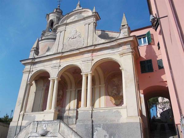 Church with arched portico, columns, bell tower, frescoed facade under blue sky