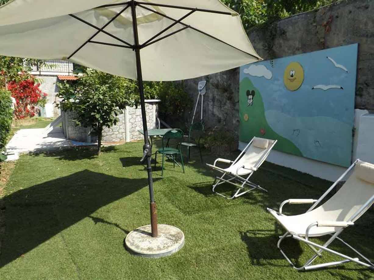 Ombrellone e sdraio su prato sintetico, muro dipinto con Topolino e sole
