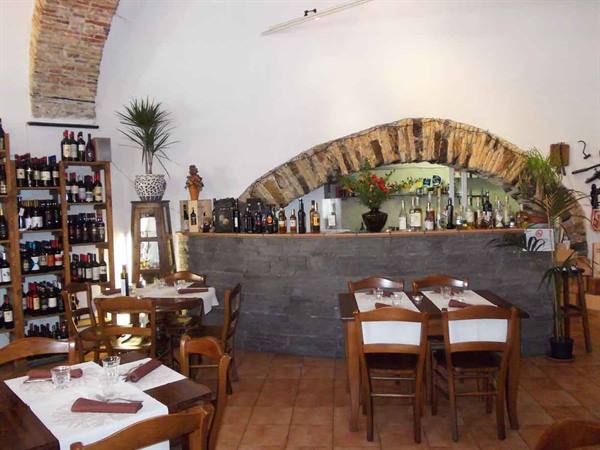 Trattoria dining room with wooden tables, wine bottles and stone arch