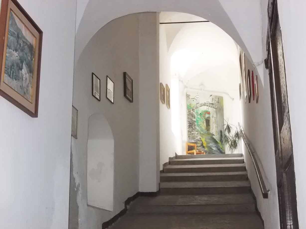 Scalone interno con arco bianco, quadri alle pareti e murale luminoso in fondo