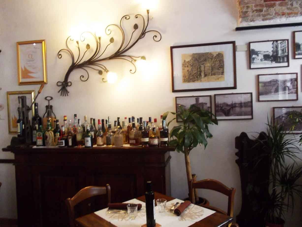 Bottega con bottiglie di vino su credenza in legno, lampada di ferro battuto e fotografie d'epoca alle pareti
