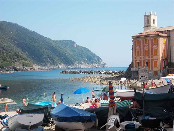 Fishing boats on San Fruttuoso beach, sunbathers under umbrellas near the abbey