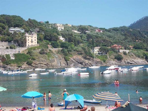 Bathers under beach umbrellas in the green bay, moored boats, houses on the hillside