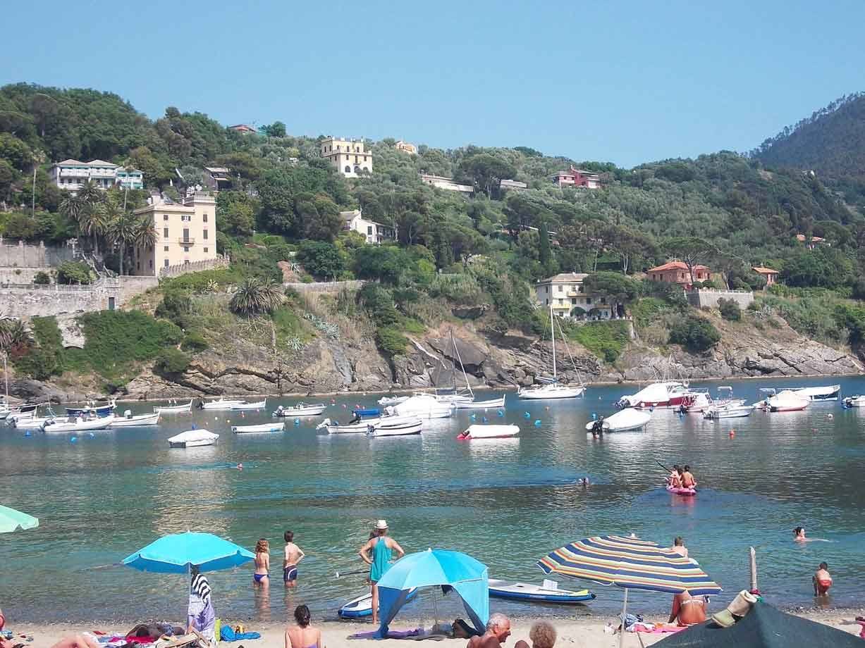 Bagnanti sotto ombrelloni nella baia verde, barche ancorate, case sulla collina