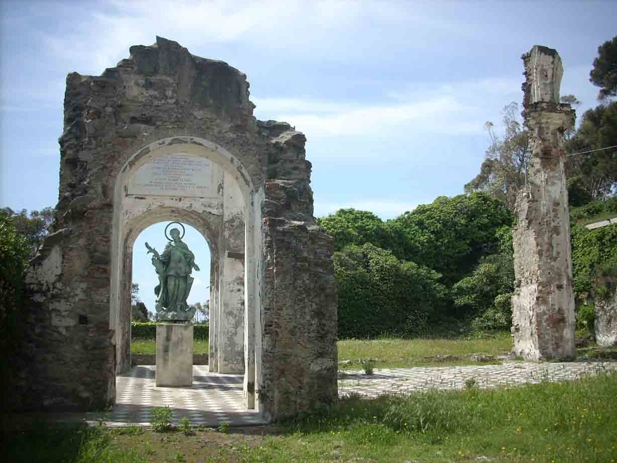 Statua bronzea sotto un arco di rovine in pietra, alberi verdi dietro